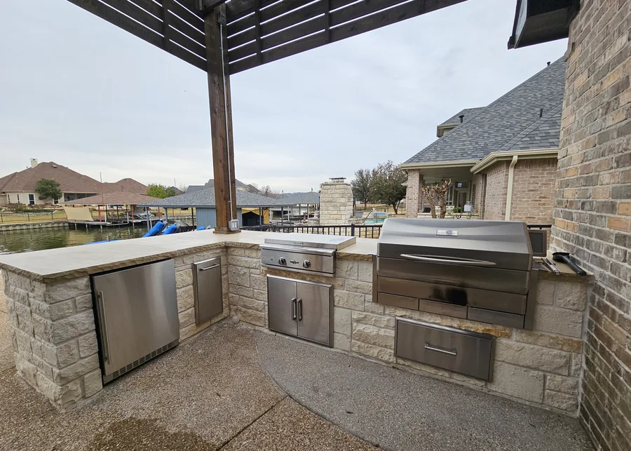 Stone masonry outdoor kitchen with built-in grill under a pergola in Fort Worth